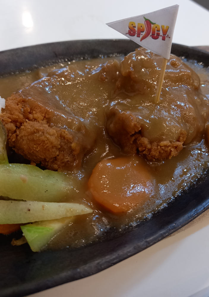 Zoom shot of Spicy Crispy Fried Chicken Fillet Drowning In Gravy with Spicy Flag and veggies on a sizzling hot plate.