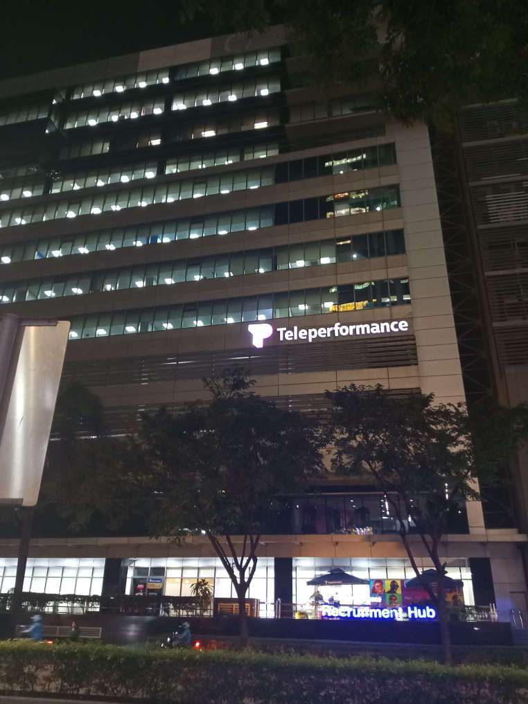 Teleperformance building at night with led outdoor signage on lower floor outer wall. On ground floor is the Teleperformance Recruitment Hub.