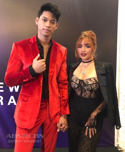 Couple of Andrea Brillantes and Ricci Rivero in an ABS-CBN party. On left is Ricci Rivero wearing a red suit and ont the right side is Andrea Brillantes wearing some kind of lace-dress topped with a blazer.